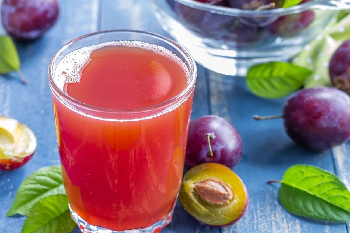 Ein Glas selbst gemachter Pflaumensaft. Drumherum liegen frische Pflaumen.