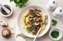 Polenta mit Pilzen auf einem weißen Teller. Daneben liegen die Zutaten und Besteck.