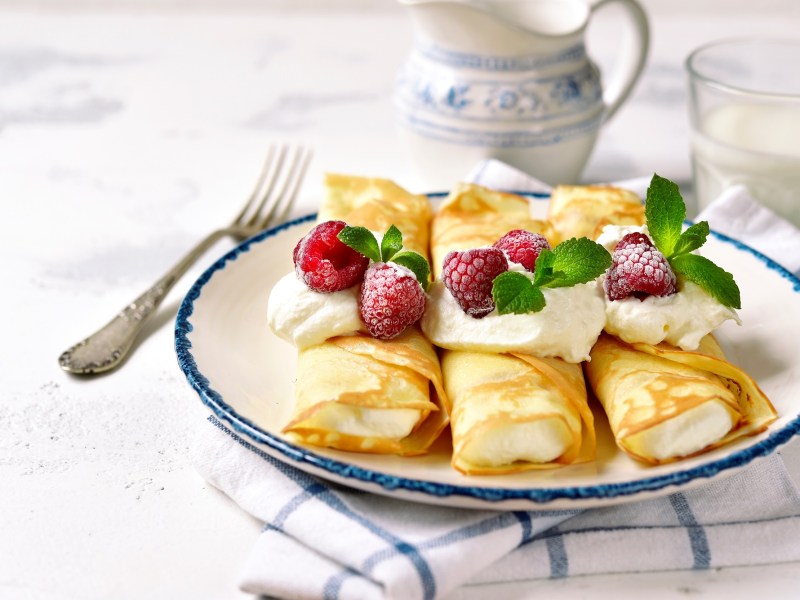 Ricotta-Pfannkuchen, garniert mit Himbeeren und Minze, auf einem Teller.