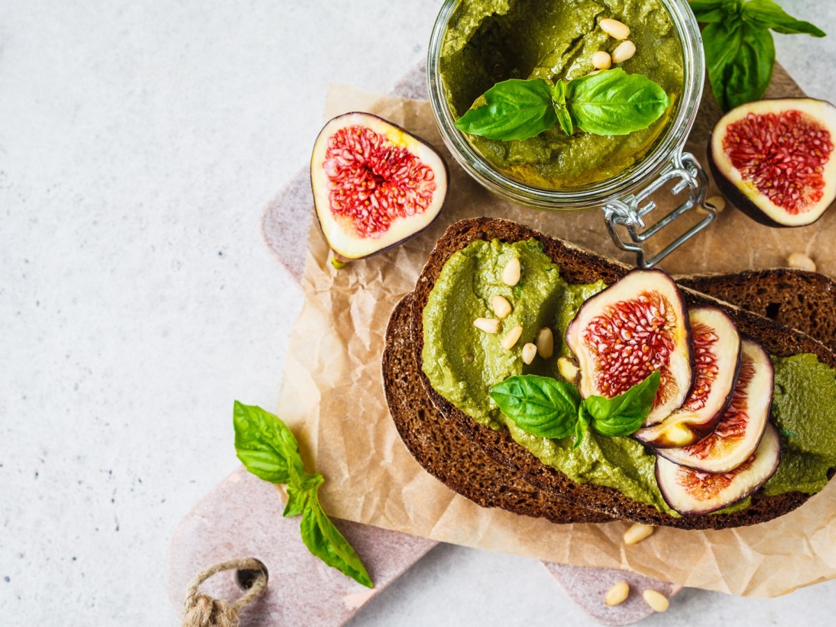 Roggenbrot mit Pesto und Feigen auf einem Brett, Glas Pesto daneben