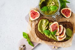 Roggenbrot mit Pesto und Feigen auf einem Brett, Glas Pesto daneben