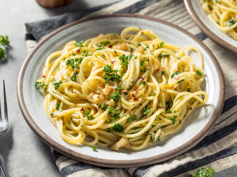 Ein Teller Spaghetti aglio e olio mit Chili und Petersilie, daneben eine Gabel.