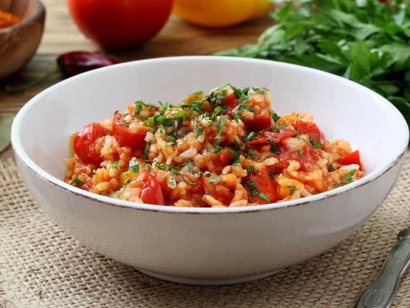 Eine Schüssel Tomatenreis mit Spinat, dahinter frische Zutaten.