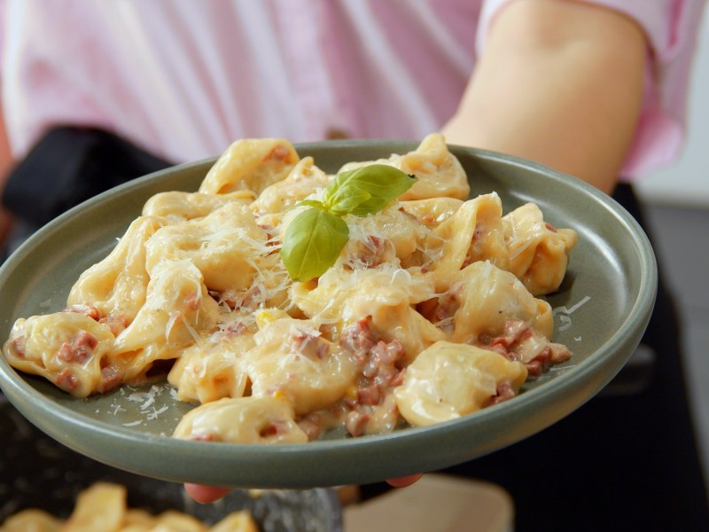 Tortellini in Sahnesoße auf einem grauen Teller.