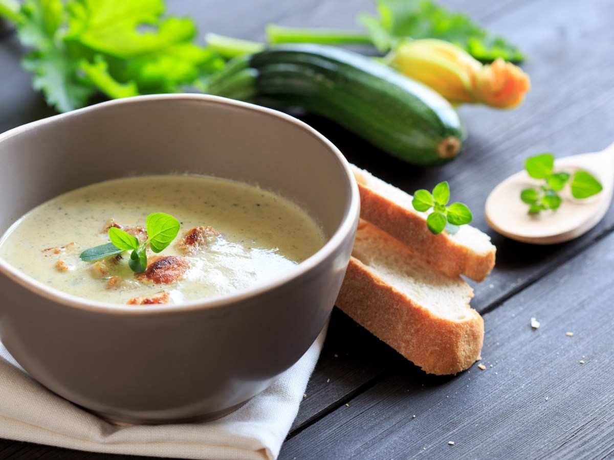 Schale mit Zucchini-Kokos-Suppe und Gemüse daneben