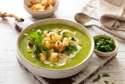 Eine Schüssel Zucchini-Spinat-Suppe mit Croûtons, Lauch, Schmand und Kräutern.