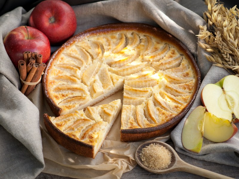 Apfel-Marzipan-Tarte auf einem Küchentuch, Äpfel daneben