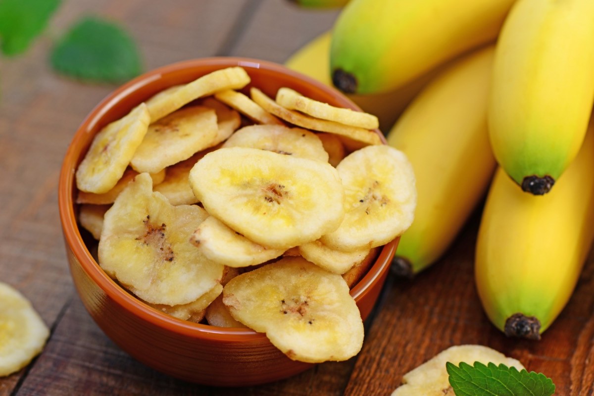 Bananenchips in einer Schüssel. Daneben frische Bananen.