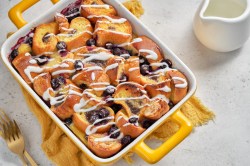 Brotauflauf mit Blaubeeren und Frosting in gelber Auflaufform.