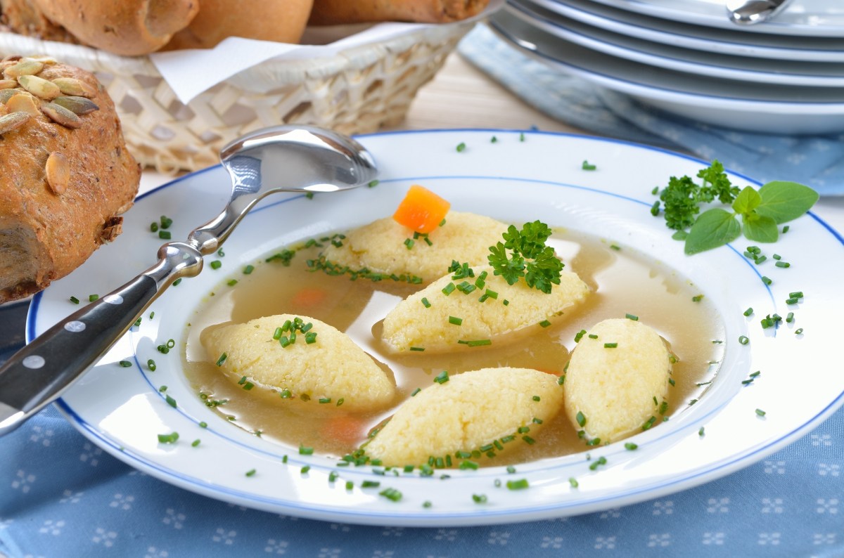 Grießschöberl-Suppe auf einem Teller, daneben ein Brötchen. Nahaufnahme.