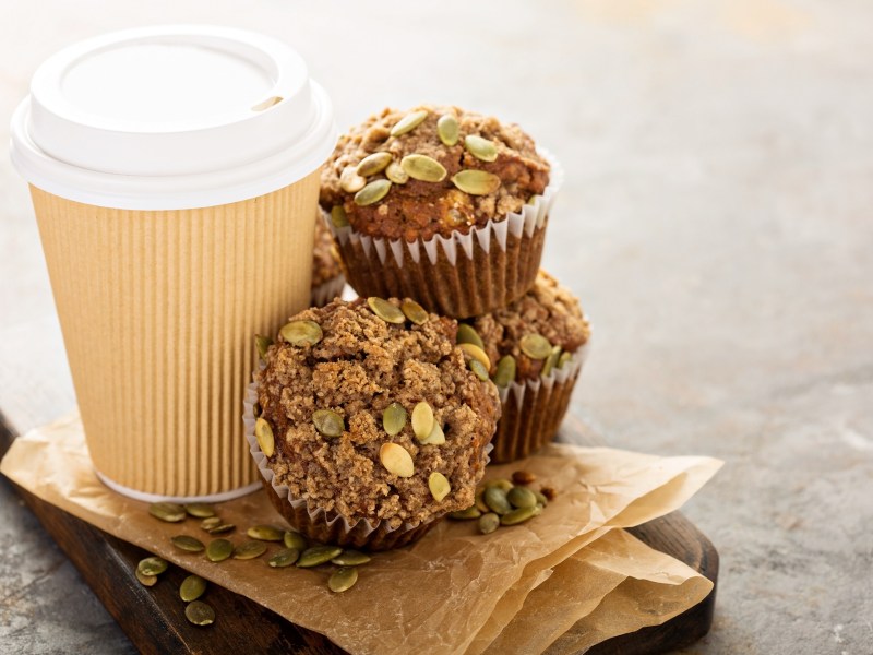 Kaffeemuffins mit Kürbiskernen neben einem Pappbecher Kaffee.