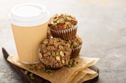 Kaffeemuffins mit Kürbiskernen neben einem Pappbecher Kaffee.