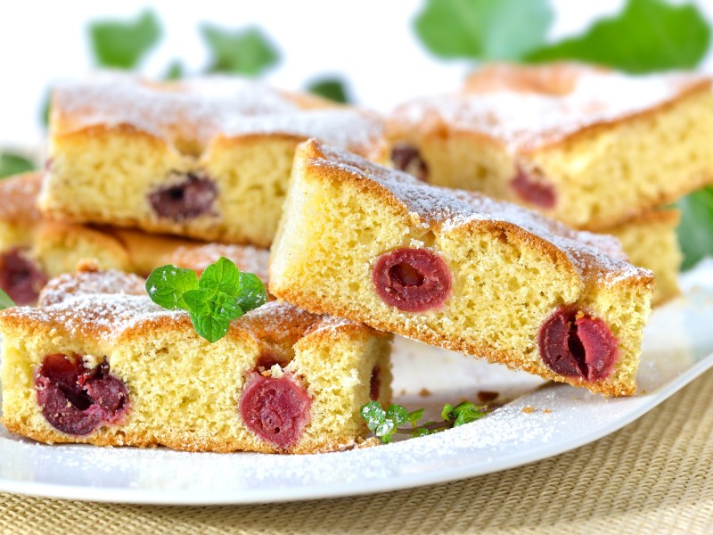 Ein Teller mit mehreren Stücken Kirschkuchen vom Blech bestreut mit Puderzucker.