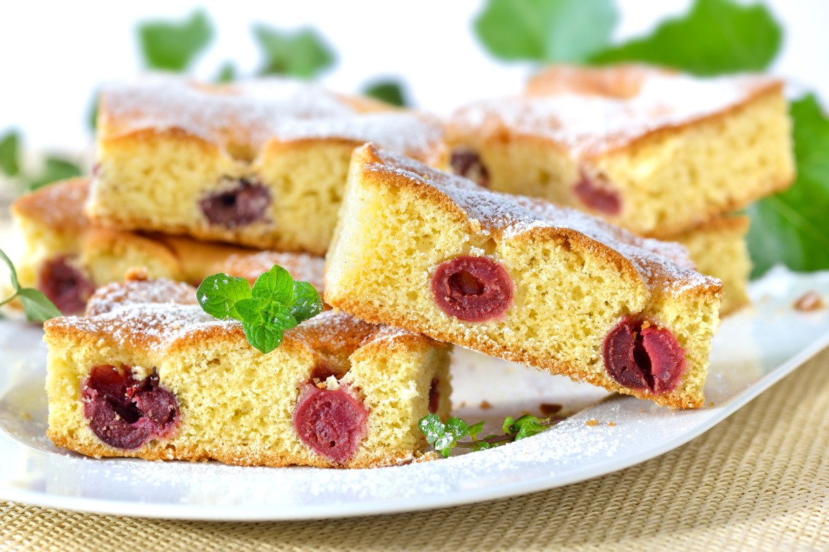 Ein Teller mit mehreren Stücken Kirschkuchen vom Blech bestreut mit Puderzucker.