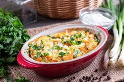 Kürbis-Gnocchi-Auflauf in ovaler, roter Auflaufform, daneben einige frische Zutaten.