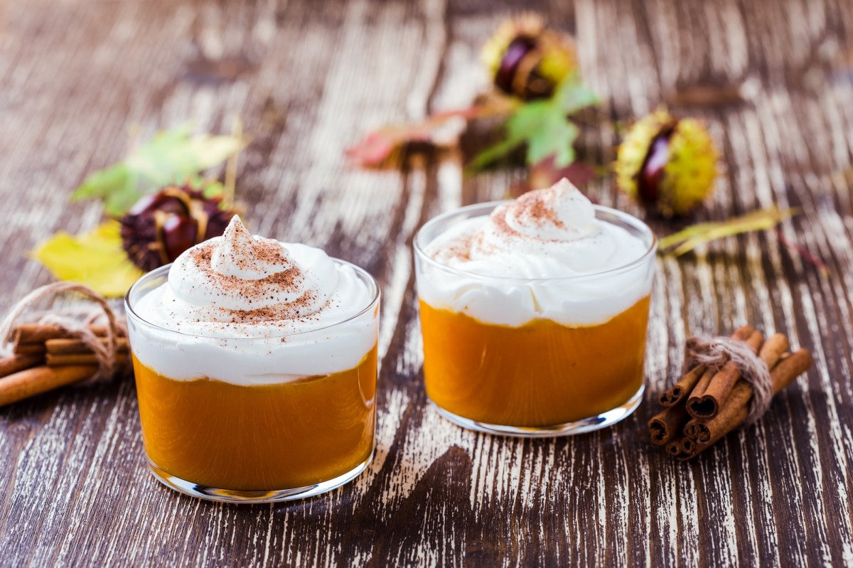 zwei Gläser Kürbis-Mousse mit Sahnehaube und Zimt bestreut, drumherum Kastanien.