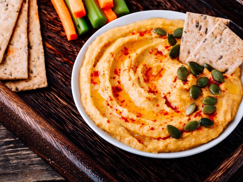 Schale mit Kürbis-Frischkäse-Dip auf Tablett, Cracker und Gemüsesticks