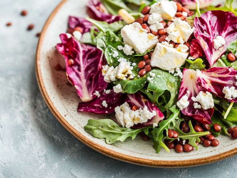 Ein Teller Rucola-Radicchio-Salat mit Linsen und Fetawürfeln. Nahaufnahme.