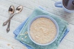 Schottischer Porridge in einer hellblauen Schüssel, daneben ligeen zwei Löffel.