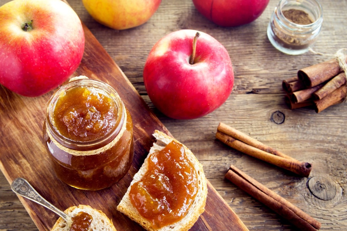 Ein Glas Bratapfelmarmelade. Daneben frische Äpfel und ein Brot mit Marmelade bestrichen.