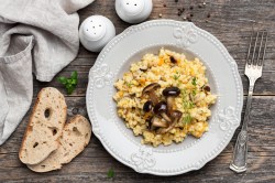 Ein Teller Graupenrisotto mit Pilzen. Daneben liegen zwei Scheiben Brot.