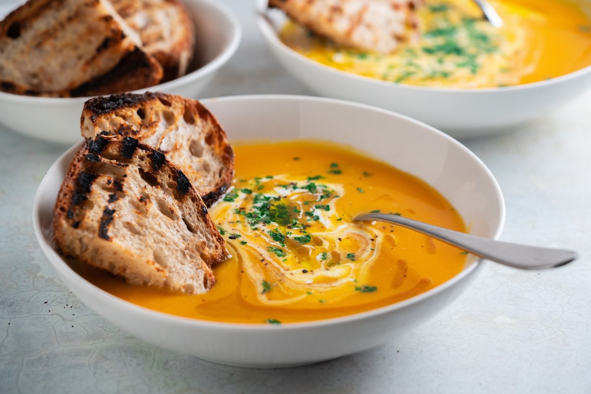 Eine Schüssel Kokos-Kürbissuppe mit Orangensaft und Brotscheiben.