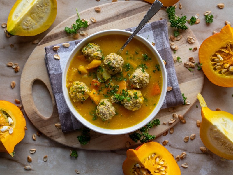 Eine Schüssel Kürbissuppe mit Hackbällchen. Daneben liegen angeschnittene Kürbisse.