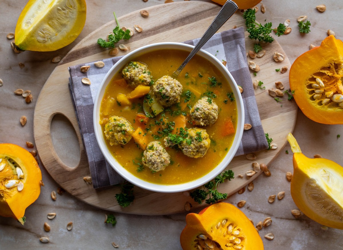 Eine Schüssel Kürbissuppe mit Hackbällchen. Daneben liegen angeschnittene Kürbisse.