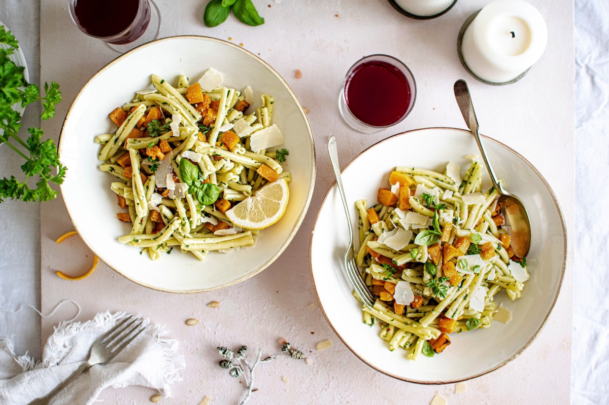 Zwei Teller Nudeln mit Kürbis und Pesto, serviert mit Parmesan.