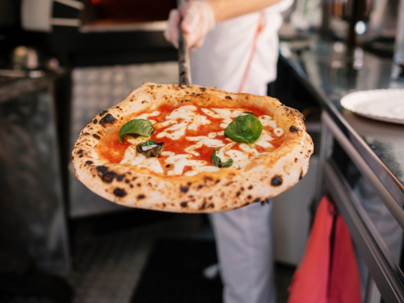 Perfekte Pizza: Ein Pizzabäcker präsentiert eine fertige Pizza.