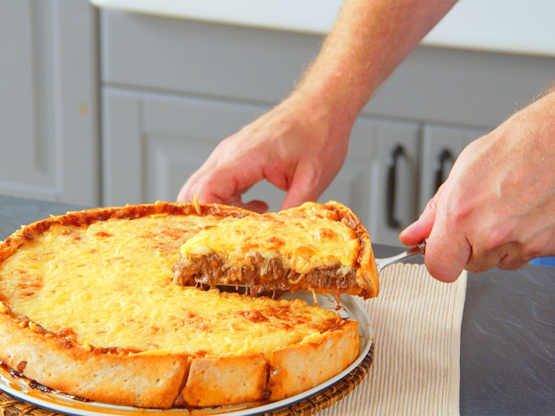 TiefkÃ¼hlpizza-Kuchen, aus dem ein StÃ¼ck herausgenommen wird.