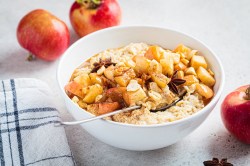 Eine Schale Bratapfel-Porridge mit gebratenen Äpfeln und Anissternen, drumherum Äpfel.