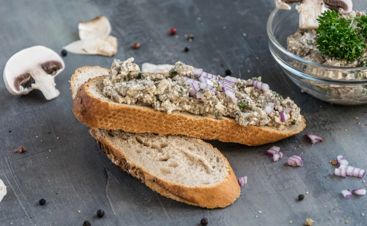 Scheibe Brot bestrichen mit Champignon-Zwiebel-Aufstrich und eine Schale mit dem Aufstrich dahinter