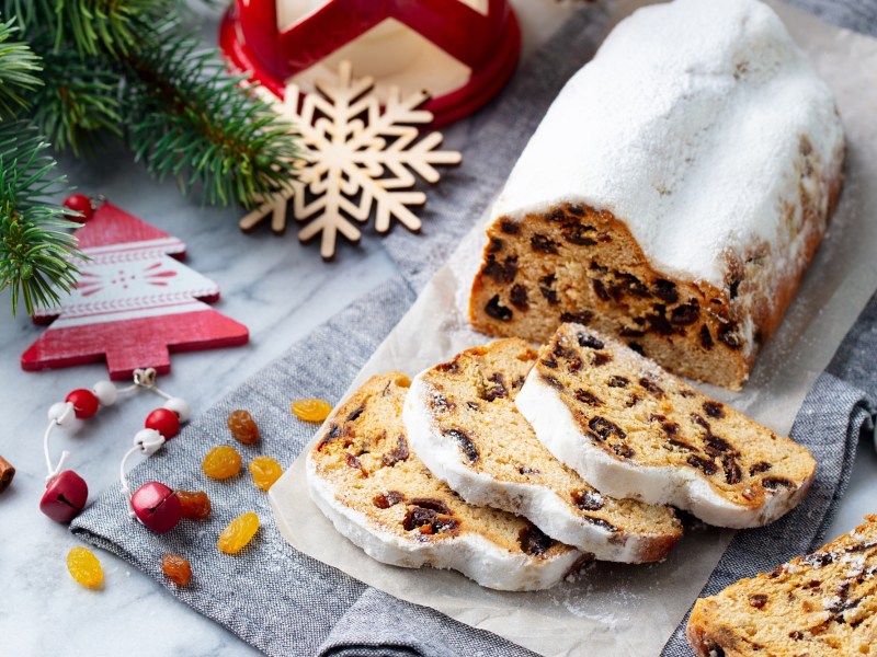 Christstollen-Rezept: ein angeschnittener Stollen mit Puderzucker bestreut, drumherum etwas Weihnachtsdeko.