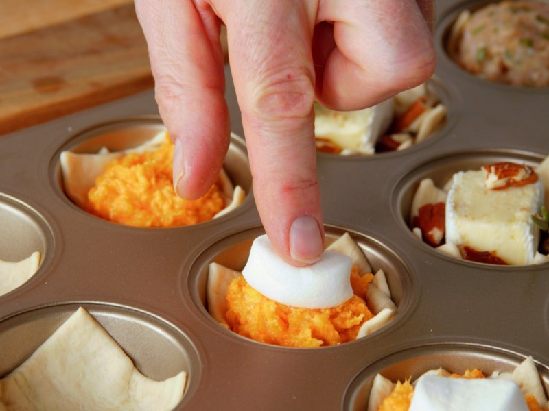 Fingerfood-Cups: Ein Marshmallow wird auf Kartoffelbrei aus Süßkartoffel in einem Muffinblech gedrückt.