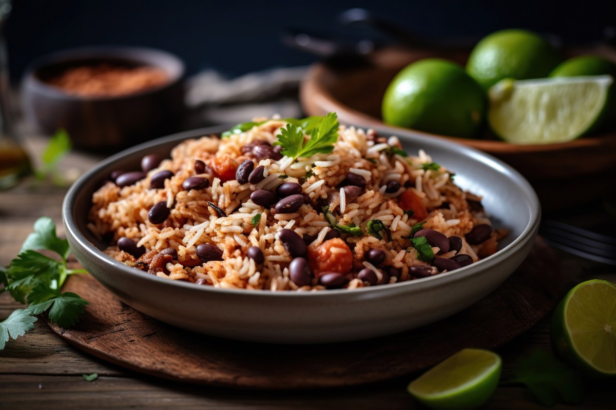 Eine dunkle Schale mit Gallo Pinto. Daneben liegen Limetten.