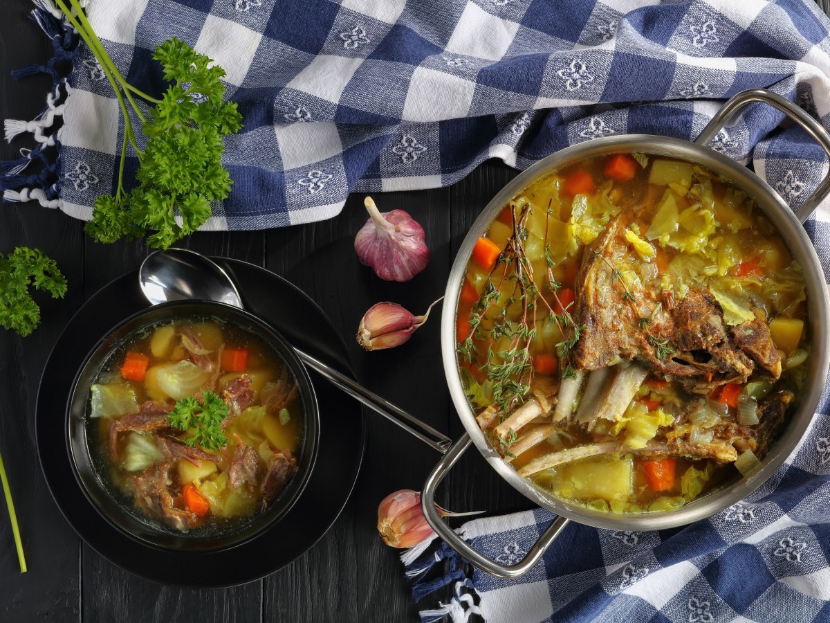 Ein Topf und eine Schale Kjötsupa: isländische Lammsuppe mit Kohl auf einem karierten Geschirrtuch.