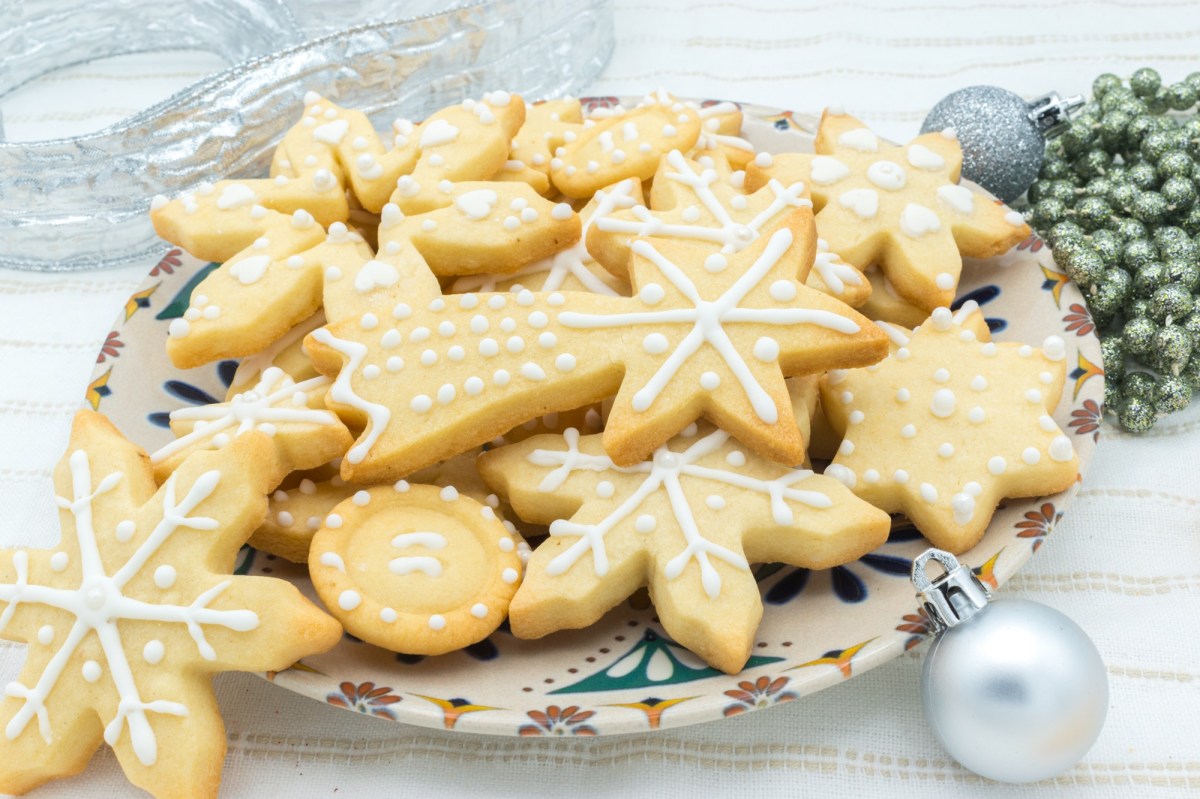 Ein Teller Marzipanplätzchen verziert mit Zuckerguss, daneben Weihnachtsdeko.