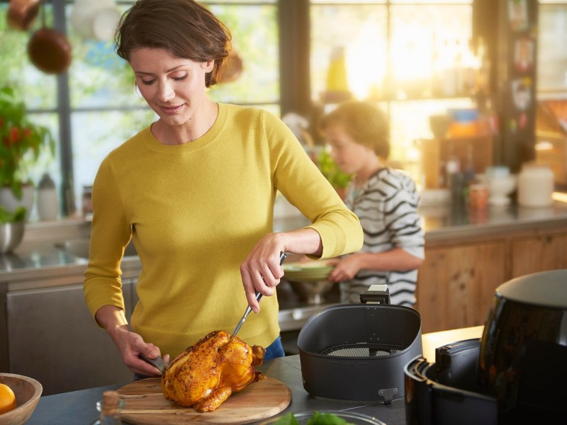 Philips Airfryer XL Black Friday Amazon: Frau kocht mit Heißluftfritteuse ein Huhn.