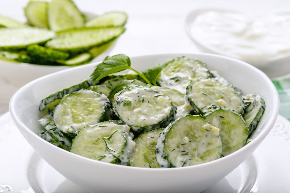 Eine Schale Mizeria, polnischer Gurkensalat mit Dill und Sourcream. Im Hintergrund eine Schale Gurkenscheiben,