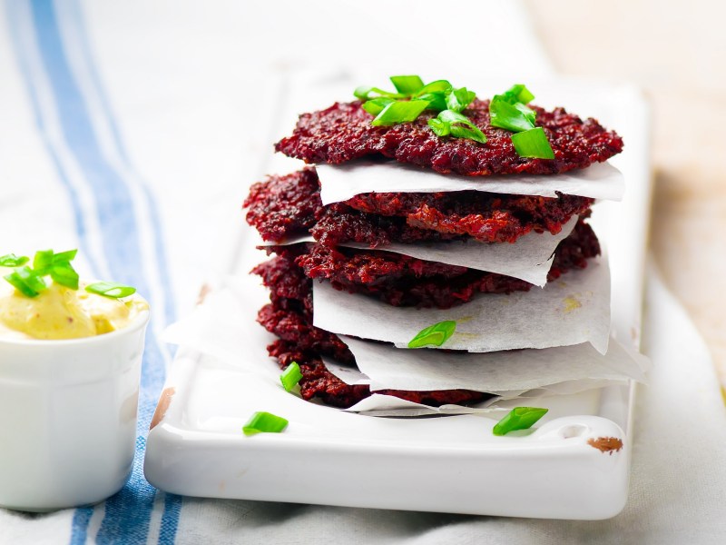 Ein Stapel Rote-Bete-Puffer auf einer weißen Unterlage, getrennt von kleinen Stücken Backpapier.