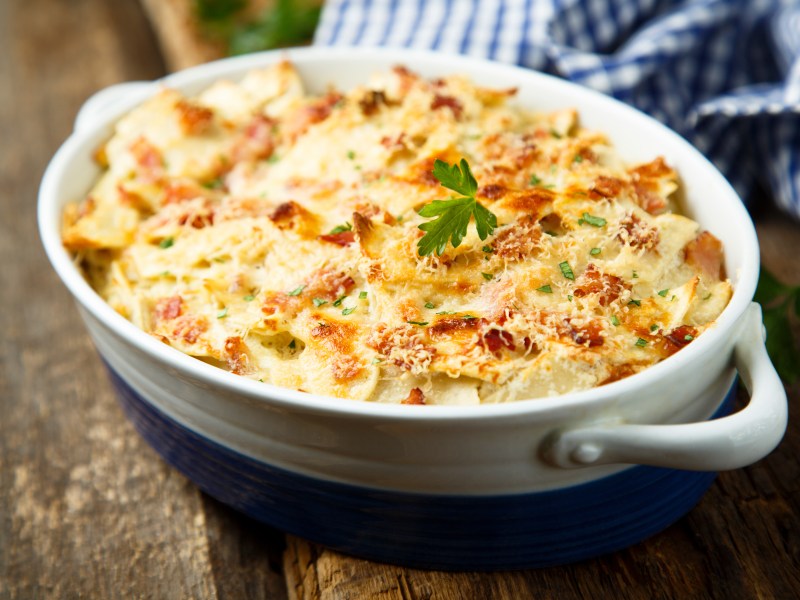 Spitzkohl-Lasagne in ovaler Auflaufform, daneben ein kariertes Geschirrtuch.