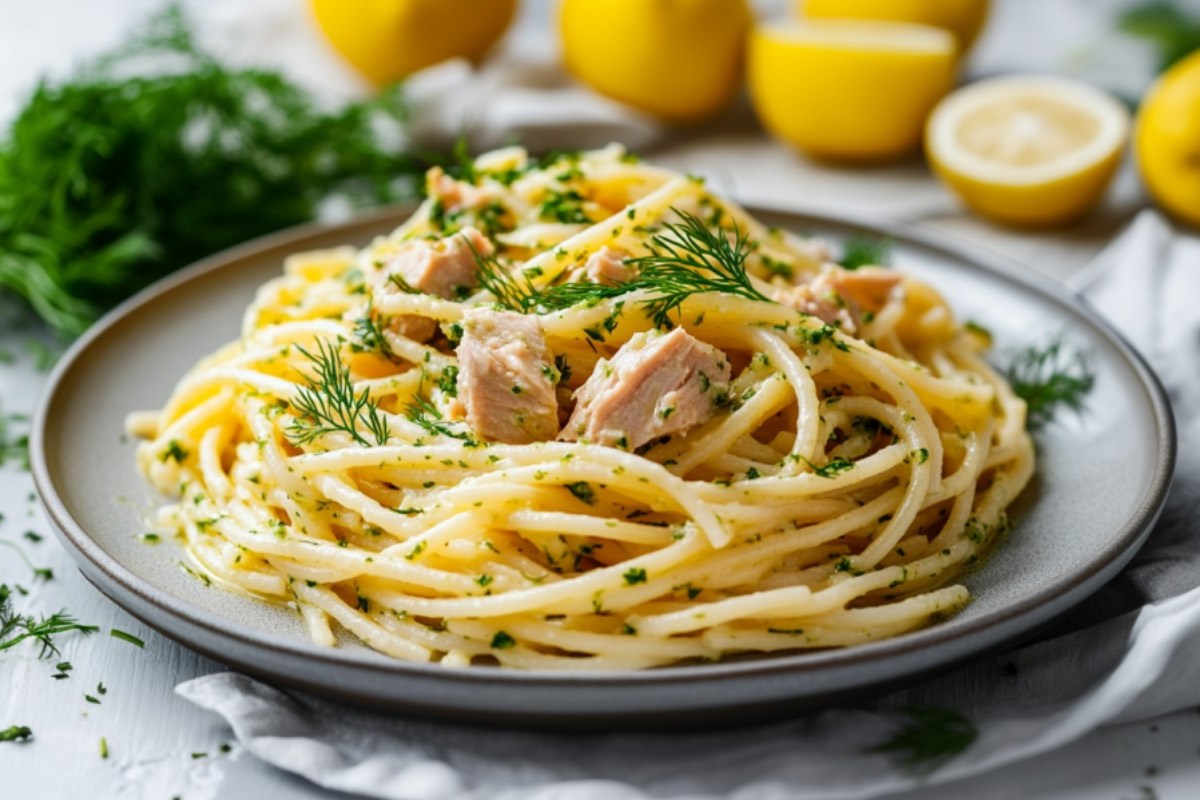 Ein Teller Thunfisch-Zitronen-Pasta mit Dill-Pesto. Im Hintergrund sind frische Zutaten zu sehen.