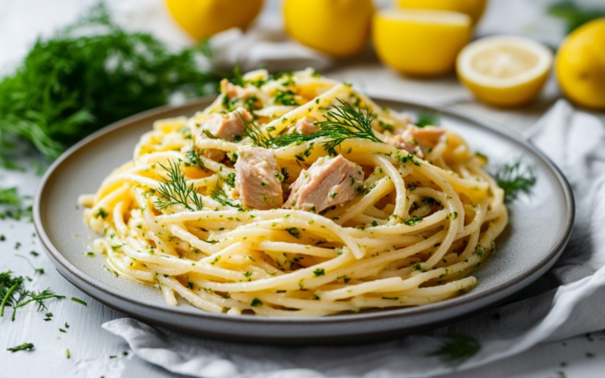 Ein Teller Thunfisch-Zitronen-Pasta mit Dill-Pesto. Im Hintergrund sind frische Zutaten zu sehen.