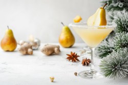 Ein Glas Birnen-Martini mit Birnen im Hintergrund und winterlichen Gewürzen