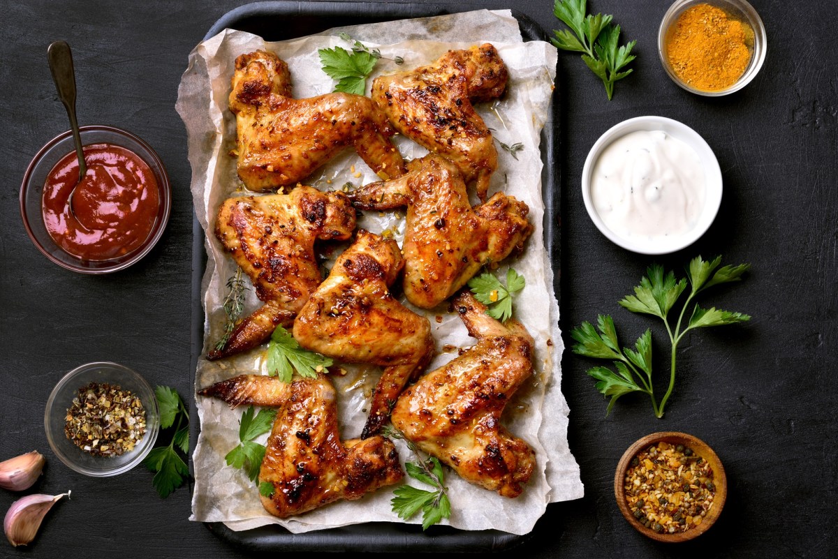 Honig Chicken Wings auf einem mit Backpapier ausgeschlagenen Backblech. Daneben stehen SchÃ¼sseln mit SoÃŸe.