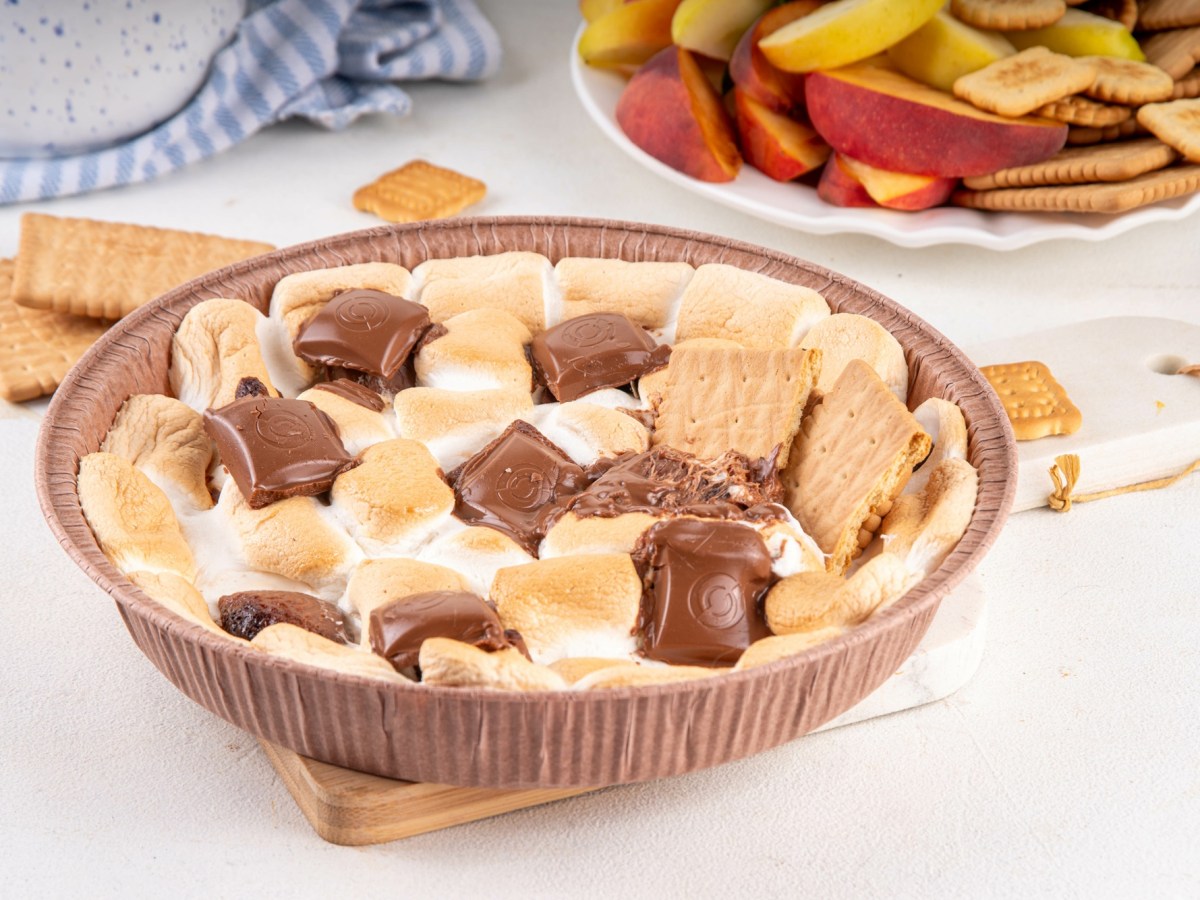 Marshmallow-Creme aus dem Airfryer mit Schokolade und Keksen in einer Pappform, daneben eine SchÃ¼ssel Obst.