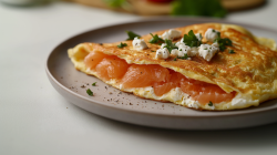 Ein Omelett mit Lachs und Feta auf einem Teller, im Hintergrund unscharf einige Zutaten.