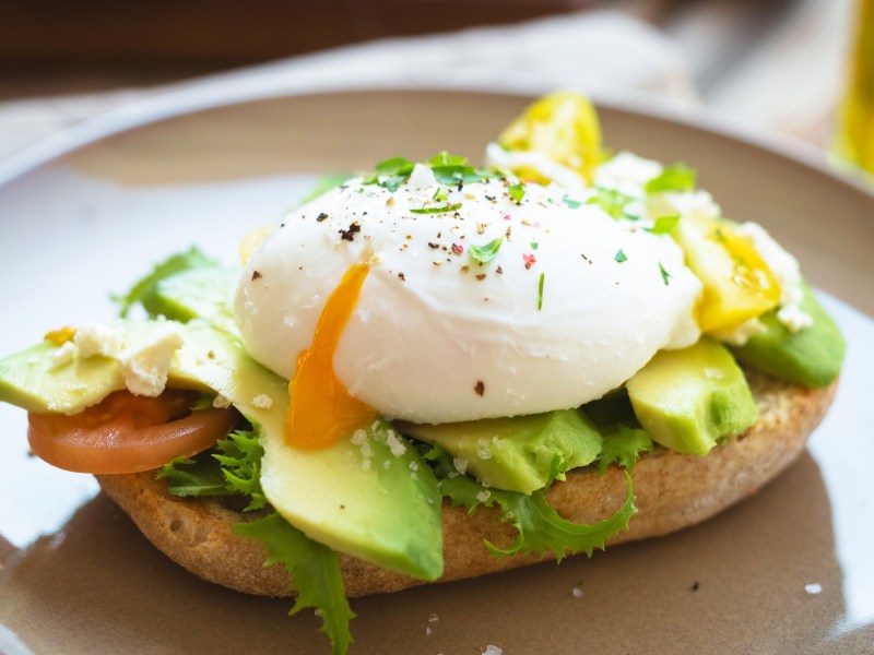 Ein Teller mit einem halben BrÃ¶tchen, auf dem Avocado und ein pochiertes Ei aus der HeiÃŸluftfritteuse liegen. Nahaufnahme.