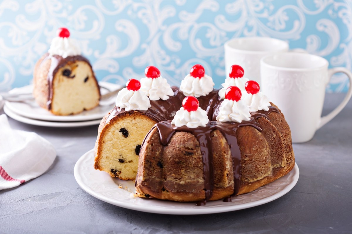 Sauerrahmkuchen auf einem weiÃŸen Teller, garniert mir Sahne und Kirschen.